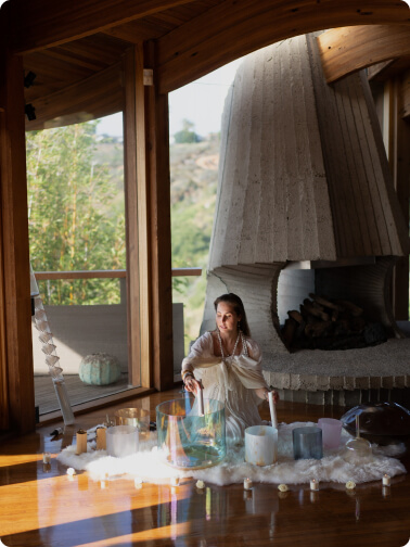 a girl seating inside in font big window, surrounded with sound healing bowls