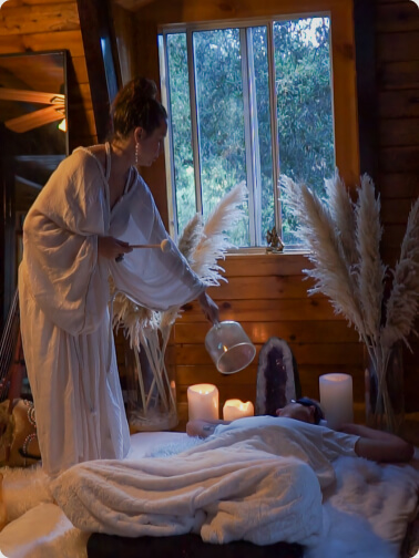 a girl with a sound healing bowl standing on top of a person laying down under the blanket