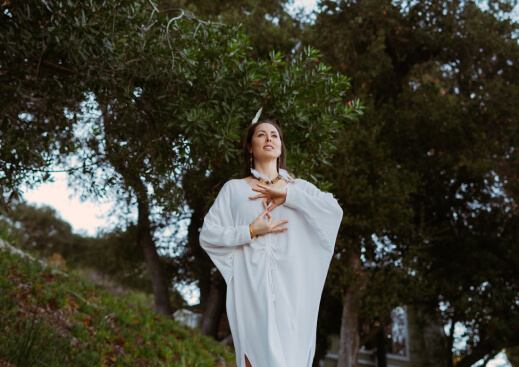 girl in a white dress stending in trees with a closed eyes