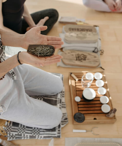 person holds a cup of raw team leaves and a wooden try with tea cups