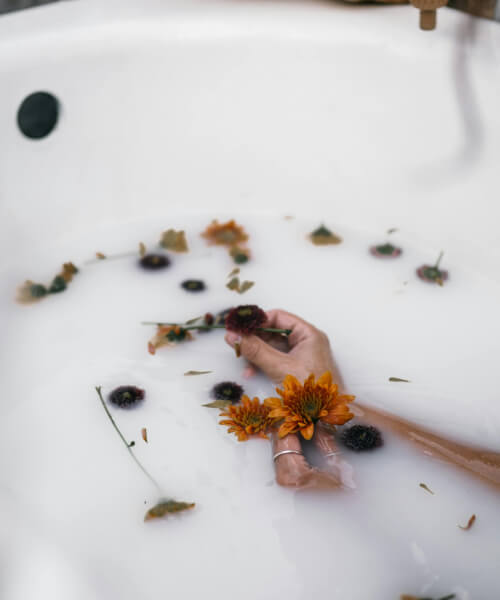 girl lays in a bathtub full on milky colored water and a some flowers