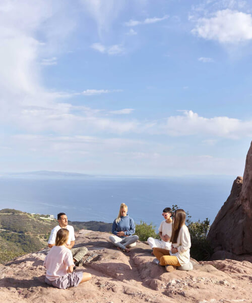 group of people are seating outside in a lotus poses