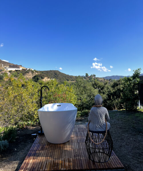 a bath standing on a wooden pallet facing mountain view with a buddha next to it